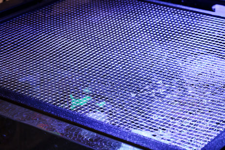Close view of clear quarter-inch mesh locked into a black Keepr 3D-printed aquarium lid frame under reef lighting